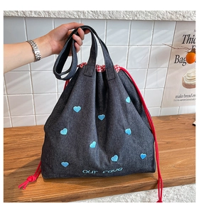 Detailaufnahme der Herzstickerei auf Denim-Tote mit rotem Kordelzug und Karofutter