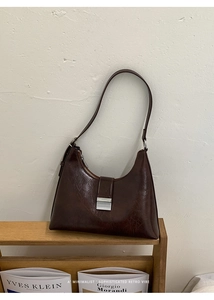 Detailed close-up of dark brown vintage underarm bag with silver buckle on wooden shelf