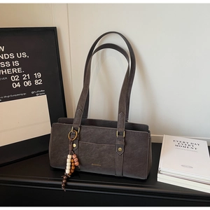 Detail of grey shoulder bag with wooden bead tassel and ZHCNMA logo on matte leather