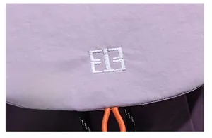Macro shot of white EIE embroidery on light purple fabric with orange drawstring detail