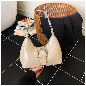 Vue détaillée du sac beige brillant avec boucle ronde argentée sur un sol texturé