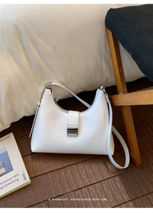 Detail of white wrinkled leather hobo bag with silver buckle on dark wood floor