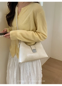 Detail of a minimalist cream shoulder bag with glossy finish and silver buckle on a model