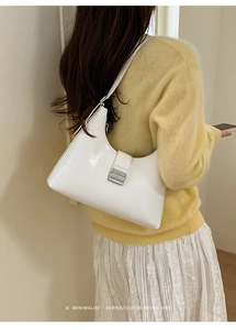 Close-up of minimalist white patent leather hobo bag with silver buckle on a model