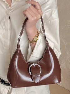 Sac hobo marron foncé brillant avec boucle fer à cheval argenté porté à l'épaule chic