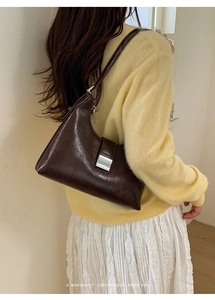 Detail of a dark brown retro underarm bag with silver metal buckle on a model