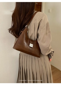 Minimalist dark brown leather tote bag with silver buckle worn as a shoulder bag