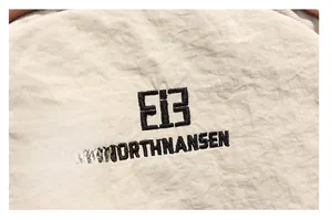 Close-up of beige fabric texture with black embroidered logo and fine stitching details