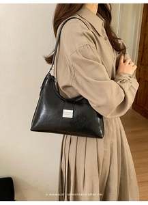 Detail of retro black pleated leather bag showing silver metal buckle and oil-wax texture