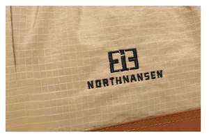 Detail of khaki plaid fabric with black embroidered logo and durable brown leather trim
