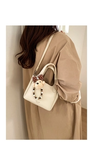 Detailed side view of white lychee pattern bucket bag with cute bear charm on a model
