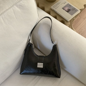 Detail of black glossy hobo bag with silver metal buckle on a white sofa scene