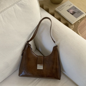 Detailed view of brown oil wax leather shoulder bag with vintage metal buckle on sofa