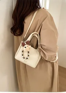 Detail view of cream white bucket bag with pebble leather texture and a cute plush bear charm