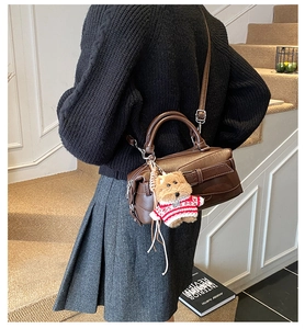 Détail d'un sac Boston marron foncé avec coutures géométriques et breloque petit ours
