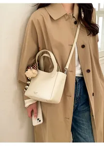 Detail view of off-white bucket bag with plush dog charm worn with a classic khaki coat