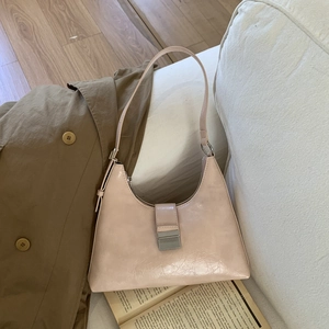 Detail of a beige pleated faux leather hobo bag with silver buckle on a cozy white sofa