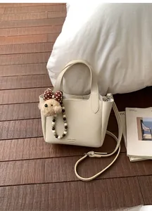 Close-up of creamy white lychee grain leather bucket bag with cute bear charm and beads