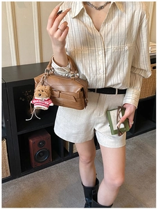 Brown leather crossbody bag detail with a cute teddy bear charm in a cozy indoor scene