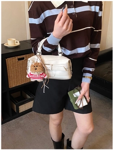 Close-up of white crossbody pillow bag with cute brown bear plush charm accessory