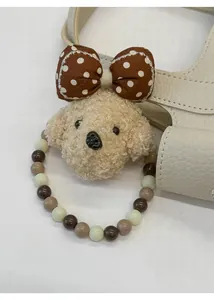 Detail of a curly beige plush poodle charm with a polka dot bow on a leather bag