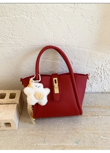 Dettaglio borsa rossa texture litchi con fibbia dorata e ciondolo in peluche bianco