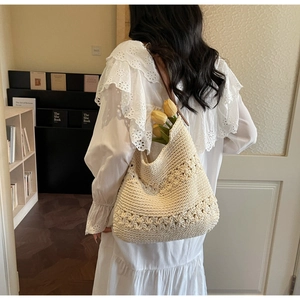 Dettaglio della borsa tote all'uncinetto crema con manici in pelle marrone indossata a spalla