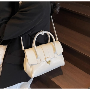 Detailaufnahme einer weißen Handtasche mit goldener Schnalle zu einem schwarzen Anzug