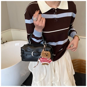 Detail of a vintage black leather handbag featuring a cute brown plush bear charm accessory