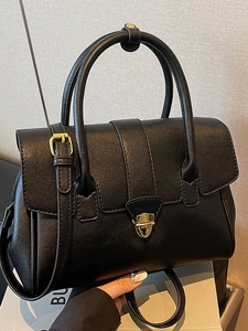 Minimalistische schwarze Lederhandtasche mit goldener Schnalle und Zylindergriff in 45-Grad-Ansicht