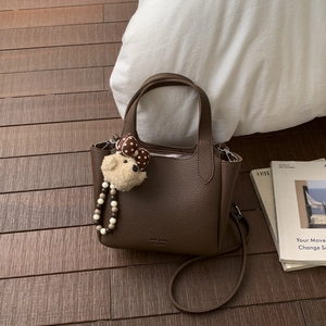 Close-up of dark brown lychee texture leather handbag with cute plush bear charm detail
