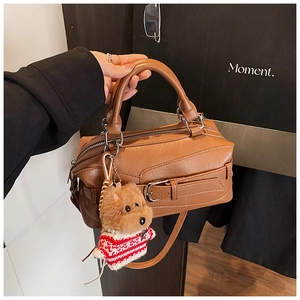Close-up of brown vintage Boston bag featuring a cute teddy bear plush charm and fine texture