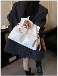 Close-up of a white canvas drawstring bucket bag with cute bear charm and pocket details