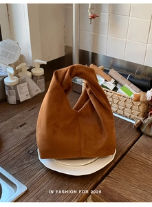 Detail of caramel suede-like dumpling bag with unique twisted handle on tiled surface