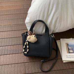 Detail of black pebbled leather handbag with plush bear charm and beaded pendant accessory