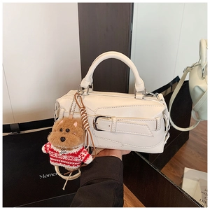 Detail of cream pillow handbag with wide decorative buckle and plush dog charm