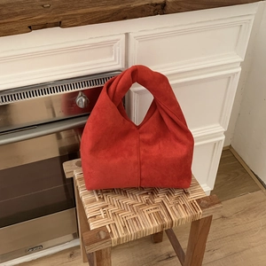 Detail of a bright red suede knot bag with a unique twisted handle on a wooden chair