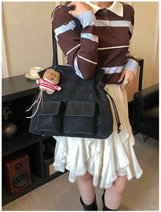 Detail of black tote bag with dual pockets and plush bear charm in a lifestyle setting