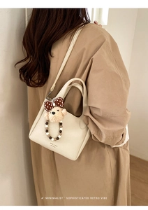 Detail of cream white pebbled leather bag with cute teddy bear charm and logo
