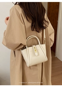 Dettaglio borsa tote in pelle color crema con chiusura dorata su un trench coat beige