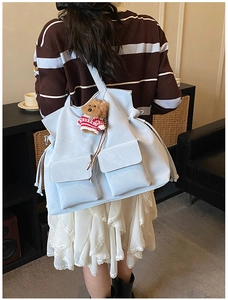Detail view of light blue tote bag with front square pockets and a cute bear charm