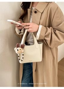 Detail view of cream bucket bag with lychee texture leather and a cute teddy bear charm