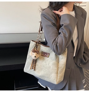 Detail of large khaki tote bag with bear motifs, plush charm and metal chain strap