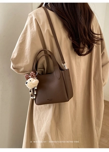 Detail of a dark brown pebble grain leather handbag with a cute plush bear charm on a model