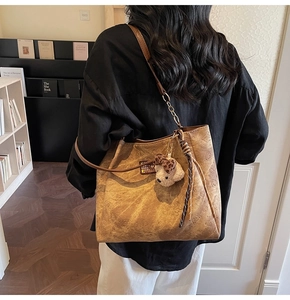Detail of a brown textured tote bag with bear embossing and a plush charm on a shoulder
