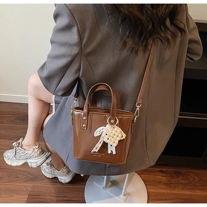 Detail of a brown patent leather bucket bag featuring lace bow and pearl charm accessories