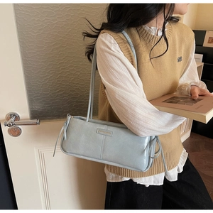 Close-up of light blue matte leather underarm bag with side drawstring details and thin straps