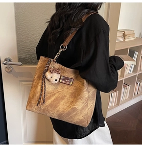 Detail of large brown tote bag with embossed bear pattern and fuzzy charm pendant