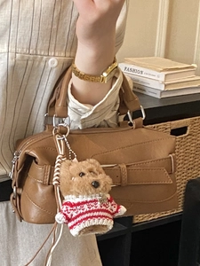 Brown vintage leather pillow bag with a plush dog charm and broad strap detail