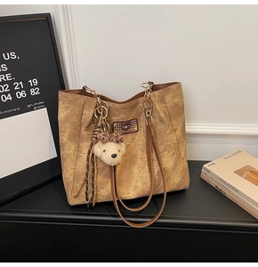 Close-up of brown suede tote bag with embossed bear pattern and plush bear charm